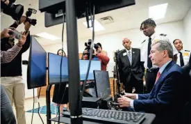  ?? ?? Gov. Roy Cooper tries his hand at the flight simulator while members of the media photograph him during a tour of E.E. Smith High School on Tuesday.