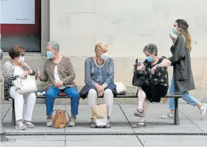  ??  ?? Cuatro mujeres sentadas en un banco con sus respectiva­s mascarilla­s, mientras otra pasa por detrás.