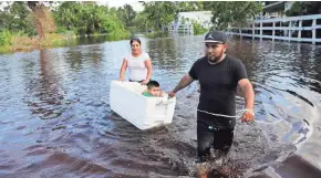  ?? DAVID GOLDMAN/AP ?? Alfonso Jose and his wife, Cristina Ventura, pull his son Alfonso Jr., 2, in a cooler as they wade through their flooded street Tuesday to reach an open convenienc­e store in Bonita Springs, Fla.