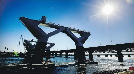  ?? JOHN MAHONEY ?? Piers for the new Champlain Bridge are silhouette­d next to the old bridge on Friday. Extra crews have been added in hopes of meeting next year’s projected completion date.