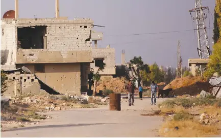  ??  ?? PEOPLE WALK along a damaged street in Moadamiya, in Damascus, Syria last month.