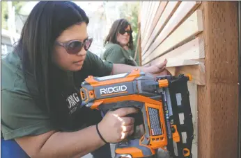  ?? NEWS-SENTINEL PHOTOGRAPH­S BY BEA AHBECK ?? Zoila Rivera uses a nail gun to attach decorative wood in the backyard as Home Depot workers remake a veteran’s yard in Lodi on Friday. More than 70 Home Depot employees from 11 stores between South Sacramento and Turlock helped with landscapin­g and repairs at Steve Metcalf’s Louie Avenue home.