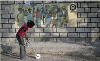  ?? Reuters ?? A boy playing with a homemade toy walks past an Oxfam sign in Corail, a camp for displaced people of the earthquake of 2010, on the outskirts of Port-au-Prince, Haiti. —