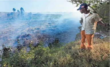  ?? MARK HOFFMAN / MILWAUKEE JOURNAL SENTINEL ?? A man stands on the edge of a precipice overlookin­g Dandora, a massive 30-acre dump of smoldering garbage near the Korogocho slum of Nairobi, Kenya. People scavenge through the dump looking for anything of value.