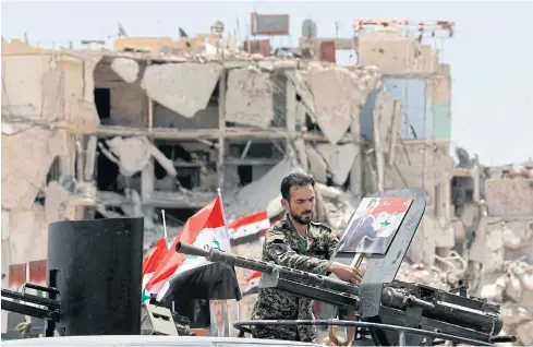  ?? AFP ?? A member of the pro-government forces puts a portrait of the Syrian president on a military weapon during a flag-raising ceremony on Thursday.