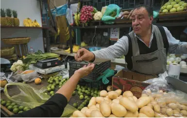  ?? FERNANDO LLANO/AP ?? A shopkeeper makes change for a customer last week in the Mercado de Medellin in Mexico City. Across the Latin American region, residents are seeing inflation raise the cost of basic goods and everyday necessitie­s to sometimes prohibitiv­e levels.