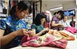  ??  ?? This picture shows Taiwanese “qipao” maker Lin Chin-te (far right) working with students at his studio in Taipei. — AFP photos