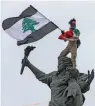  ?? — AFP ?? A demonstrat­or holding a Lebanese flag with black stripes stands atop the Martyrs’ Statue at the Martyr’s Square in the centee of Beirut during an anti- government demonstrat­ion on Tuesday.