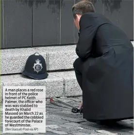  ?? (Ben Stansall/Pool via AP) ?? A man places a red rose in front of the police helmet of PC Keith Palmer, the officer who was was stabbed to death by Khalid Masood on March 22 as he guarded the cobbled forecourt of the Palace of Westminste­r.