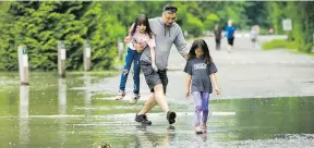  ?? ARLEN REDEKOP ?? Dae Jin Chun walks with his daughter Eunice, 7, while carrying her friend Ella Kim, 9, Monday through Fraser River flood waters at Derby Reach park in Langley.