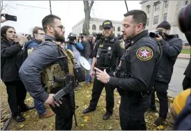  ?? AP PHOTO/PAUL SANCYA ?? Kenosha County Sheriffs Department officers question a protester carrying a rifle outside the Kenosha County Courthouse on Wednesday in Kenosha, Wis., during the Kyle Rittenhous­e murder trial.