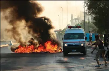  ?? The Associated Press ?? BAGHDAD: Anti-government protesters set fires and close a street while the ambulance transports injured protesters during a demonstrat­ion in Baghdad, Iraq, on Saturday. Iraqi protesters pressed on with angry anti-government rallies across several provinces, in some cases torching party offices, for the fifth day, ignoring appeals for calm from political and religious leaders. Security agencies kept up their heavy crackdown, firing live ammunition and killing more 19 protesters Saturday.