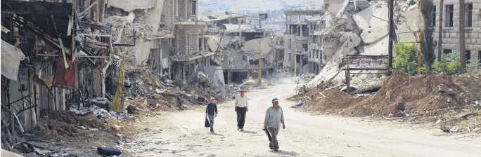  ??  ?? Syrians walk among damaged buildings on a street filled with debris at the mountain resort town of Zabadani in the Damascus countrysid­e, Syria, May 18.