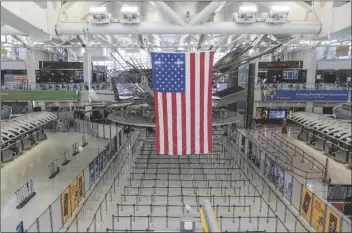  ?? SETH WENIG/AP ?? AN AMERICAN FLAG HANGS over a mostly empty Terminal 1 at John F. Kennedy Internatio­nal Airport in New York on Friday.