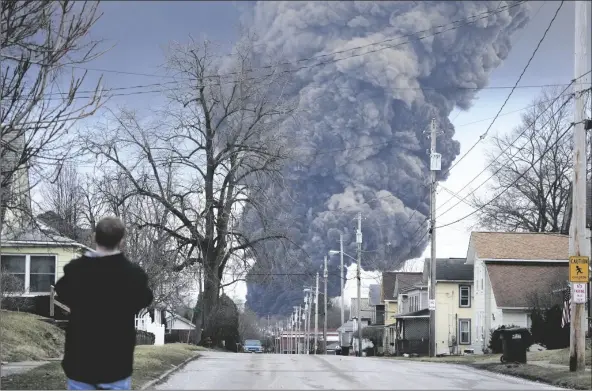  ?? GENE J. PUSKAR/AP ?? A MAN TAKES PHOTOS AS A BLACK PLUME trains Monday. rises over East Palestine, Ohio, as a result of a controlled detonation of a portion of the derailed Norfolk and Southern