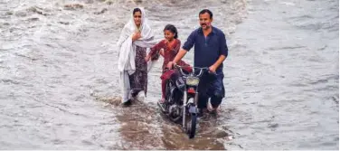  ?? Agence France-presse ?? ↑
A family wades through a flooded street after heavy rain in Karachi on Friday.