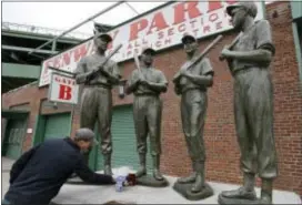  ?? STEVEN SENNE — THE ASSOCIATED PRESS ?? Trevor Lane, of Boston, places flowers at the foot of a statue of Hall of Famer Bobby Doerr, second statue from left, outside Fenway Park, Tuesday in Boston. Other statues depict Red Sox players Ted Williams, left, Johnny Pesky, second from right, and...