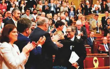  ?? AFP ?? MPs applaud after a speech by Junts per Catalonia (Together for Catalonia) MP and presidenti­al candidate Quim Torra (right) as he hugs fellow MP Elsa Artadi during a session at the Catalan parliament in Barcelona yesterday.