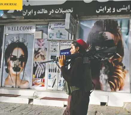  ?? WAKIL KOHSAR / AFP VIA GETTY IMAGES ?? A Taliban fighter walks past a beauty salon with images of women defaced with spray paint in Kabul's Shahr-e-naw neighbourh­ood on Wednesday.