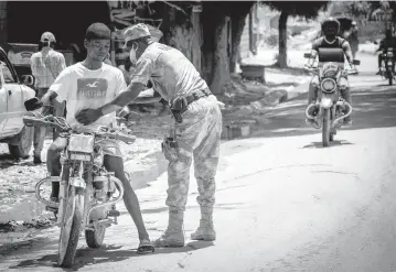  ?? JOSE A. IGLESIAS jiglesias@elnuevoher­ald.com ?? A Haitian policeman frisks a motorcycli­st at a checkpoint in Port-au-Prince.