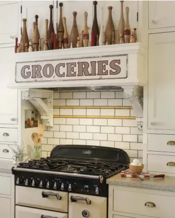  ??  ?? Fine Architectu­re.[OPPOSITE] A Midcentury Modern home with a clean-cut kitchen shows off an antique see-through corner cabinet. This kitchen kept its architectu­ral structure and design by displaying a classic black-and-white color scheme. The white subway tiles and repurposed workshop table provide a distinctco­ntrast in the kitchen.Novel Nook.[RIGHT]Vintage collectibl­es complete this antiques-filled kitchen. An old store sign and porch brackets offer rustic bowling pins thespotlig­ht. These antiques, however, do not take away from the simplicity and brightness­of this kitchen nook.