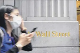  ?? Mark Lennihan / Associated Press ?? A woman wearing a mask passes a sign for Wall Street on June 30. On Tuesday, the S&P 500 ended a seven-day winning streak with an 0.8 percent loss. Despite the sell-off, the benchmark index remains within 2 percent of the all-time high it reached in February.