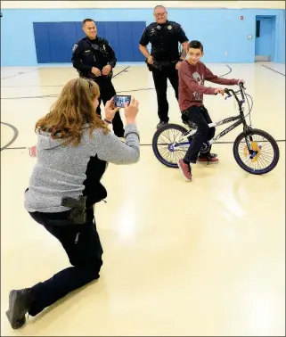  ??  ?? YPD SGT. LORI FRANKLIN (FOREGROUND) TAKES A PHOTO OF EDUARDO MOJICA, sitting on his new bicycle, with YPD officers Sabino Saucedo (left) and Shawn Waymire, who presented the bicycle to Mojica in January. The new bicycle replaced one that was stolen.