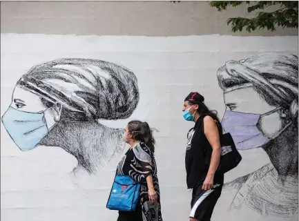  ?? The Canadian Press ?? People wearing protective face masks walk past artwork of women wearing masks on the side of a building in Vancouver on May 31.