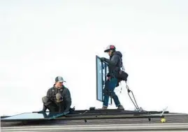  ?? TRENT SPRAGUE/CHICAGO TRIBUNE ?? Jared Salvatore, left, prepares a bracket for installati­on as Garrison Riegel of Celestar Solar positions a solar panel onto a roof in Schaumburg last November. An Aurora City Council member has proposed a program to offer a subsidy to encourage solar panel installati­on in the city.