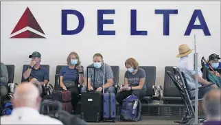  ?? RICK BOWMER — THE ASSOCIATED PRESS ?? People sit under a Delta sign at Salt Lake City Internatio­nal Airport. Delta Air Lines won’t force employees to get vaccinated, but it’s going to make unvaccinat­ed workers pay a $200 monthly health plan charge.