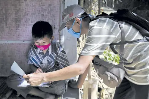  ?? AGUNG SUPRIYANTO/AGENCE FRANCE-PRESSE ?? ELEMENTARY school teacher Fransiscus Xaverius Fri Harna (right) teaches his student at the student’s home in Magelang, Central Java, after schools were closed due to the COVID-19 coronaviru­s outbreak. Some teachers are taking on dangerous terrain, bad weather and the risk of contractin­g the COVID-19 coronaviru­s, to reach home-bound students across the world’s fourth-most populous nation, home to a quarter of billion people.