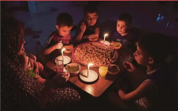  ?? AFP PIC ?? A Palestinia­n family eating dinner by candleligh­t at their makeshift home at the Rafah refugee camp, in the southern Gaza Strip, during a power outage last week. Gazans get only four hours of electricit­y supply a day.