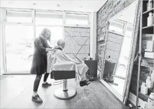  ?? GARY YOKOYAMA THE HAMILTON SPECTATOR ?? Lisa Anderson, owner of Neo Hair, gives Joan Massey a trim. She says it will take six to eight weeks to get a proper custom window pane installed after her storefront was smashed Saturday night.