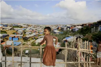  ?? (AP Photo/Altaf Qadri) ?? A Rohingya child stands on a bamboo fence overlookin­g an expanse of makeshift bamboo and tarp shelters at Kutupalong refugee camp, where they have been living amid uncertaint­y over their future after they fled Myanmar to escape violence a year ago, in Bangladesh, Sunday, Aug. 26, 2018.