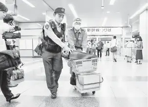  ?? — Gambar AFP ?? SIASATAN: Pegawai polis berjalan keluar membawa troli di stesen Odawara, Kanagawa semalam, selepas memeriksa kereta api berkelajua­n tinggi di lokasi kejadian bunuh.