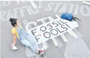  ?? AFP ?? A climate activist sits in the street with an antifossil fuel message blocking London Bridge.