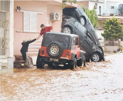  ?? — Gambar AFP ?? CEPAT NAIK!: Seorang lelaki membantu memindahka­n seorang wanita dari banjir di Mandra di barat Athens, kelmarin.