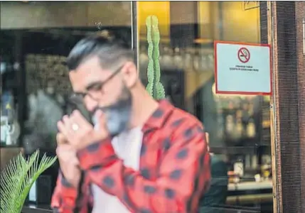  ?? WESTEND61 / GETTY ?? Un hombre enciende un cigarrillo frente a un bar con un cartel que prohíbe fumar