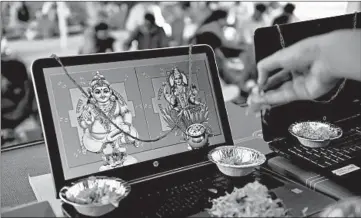  ?? SAM PANTHAKY/GETTY-AFP ?? A priest puts floral petals on a laptop displaying an image of Goddess Lakshmi, right, and Kuber Dev during Diwali, the Hindu festival of lights, Saturday near Ahmedabad, India. More than one billion Indians celebrated amid twin concerns of a resurgence in coronaviru­s infections and rising air pollution enveloping the country’s north in a cloud of toxic smog.