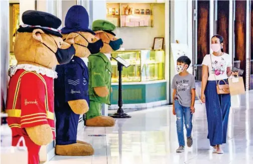  ?? Agence France-presse ?? ↑
A woman and a boy walk past Harrods’ mascot bears wearing face masks in a shopping mall in Bangkok, Thailand, on Friday.