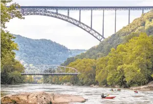  ?? TONY CENICOLA/THE NEW YORK TIMES FILE ?? Kayakers paddle by the New River Gorge Bridge in Fayettevil­le, West Virginia, in 2018. The coronaviru­s relief and spending bill passed by the federal government in December included designatin­g roughly 72,000 acres flanking 53 miles of the gorge a preserve and America’s 63rd national park.