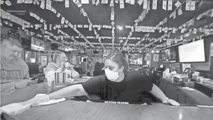  ?? RICK WOOD / MILWAUKEE JOURNAL SENTINEL ?? Bartender Carrie Boyle wipes down the bar at A.J. O'Brady's Irish Pub & Grill in Menomonee Falls on Thursday. Patrons were spaced 6 feet apart at the bar and surfaces were cleaned after every patron. In addition, the bar is taking reservatio­ns for a limited number of tables available.