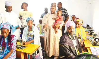  ??  ?? Governor Kashim Shettima (carrying a trainee's child) when he visited women undergoing instructor­s training in fashion design at Vodi Tailoring Institute, a private firm in Abuja engaged by the Borno State Government on Saturday.