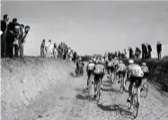  ??  ?? Fans stand high on the roadside bankings to watch as the riders pass by on the cobbles