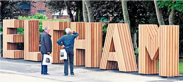  ??  ?? Civic pride: Two shoppers investigat­e the new 6ft-high wooden sign erected in Eltham High Street, by the junction with Footscray Road, in south-east London. It cost the council £40,000 but residents have called it ‘pointless’