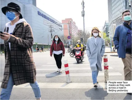  ??  ?? People wear face masks as they walk across a road in Beijing yesterday