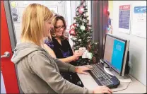  ?? MIKE HARTRANFT/RIO RANCHO OBSERVER ?? Stapleton Elementary volunteer Ginger Perez checks in using the new electronic kiosk employed by the district for security purposes. Registrar Lori Tortorici, meanwhile, retrieves the sticker with Perez’s name and photo on it.