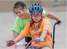  ??  ?? LEFT: Brianne Henrichs helps Josie Kohn, 12, learn to ride a bike at the camp.