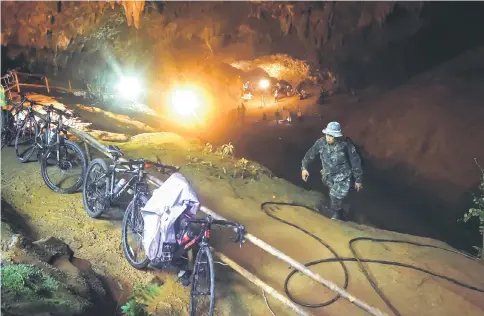  ?? — AFP photo ?? The abandoned bicycles belonging to the missing children are seen parked together while Thai rescue personnel conduct rescue operations under floodlight­s, seen in the background, at the entrance of Tham Luang cave in Chiang Rai province as the search continue for the 12 children and their coach.