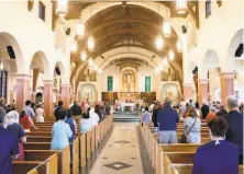  ?? Jessica Christian / The Chronicle ?? Masked worshipper­s stand socially distanced during an indoor Mass at the Church of Saint Raphael in San Rafael.